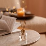 Liquid home fragrance in diffuser with open paper book on coffee table in bedroom indoors close up over scented candle. Cozy and hygge atmosphere. Aromatherapy.